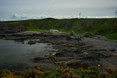 A view over a small rocky beach surrounded by green banks with some buildings at a distance