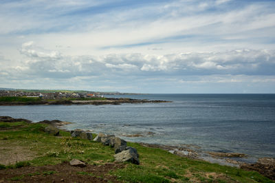A rocky beach and grass, a village at a distance - Moray Firth