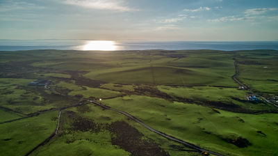 Sunset across lush fields and hills, with the sea in the backdrop.