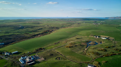 Aerial photograph of green fields and a small village with the sea in the background.