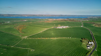 Aerial view of green fields and a small village with the sea in the distance.