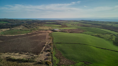 Aerial view of green and brown fields in the distance, with the sea in the distance.