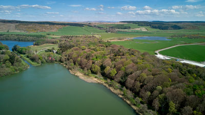 On a sunny day, an aerial shot of a lake, verdant fields, and hills.