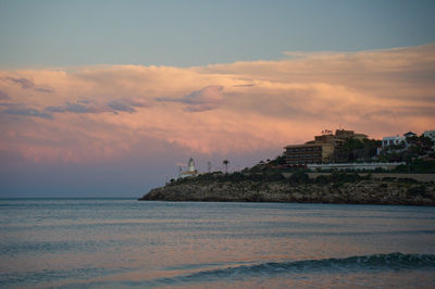 a cloudy sky at dusk with a lighthouse on a cliff in front of a body of water