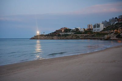 a beach at dusk with a lighthouse in the background