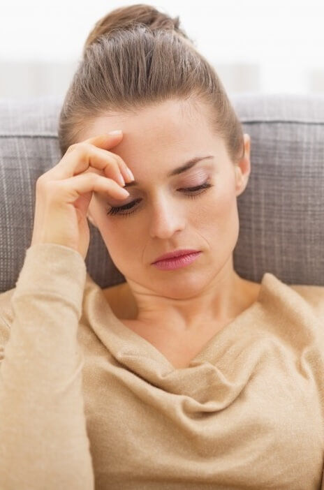 Dark-haired woman on sofa contemplating menopause