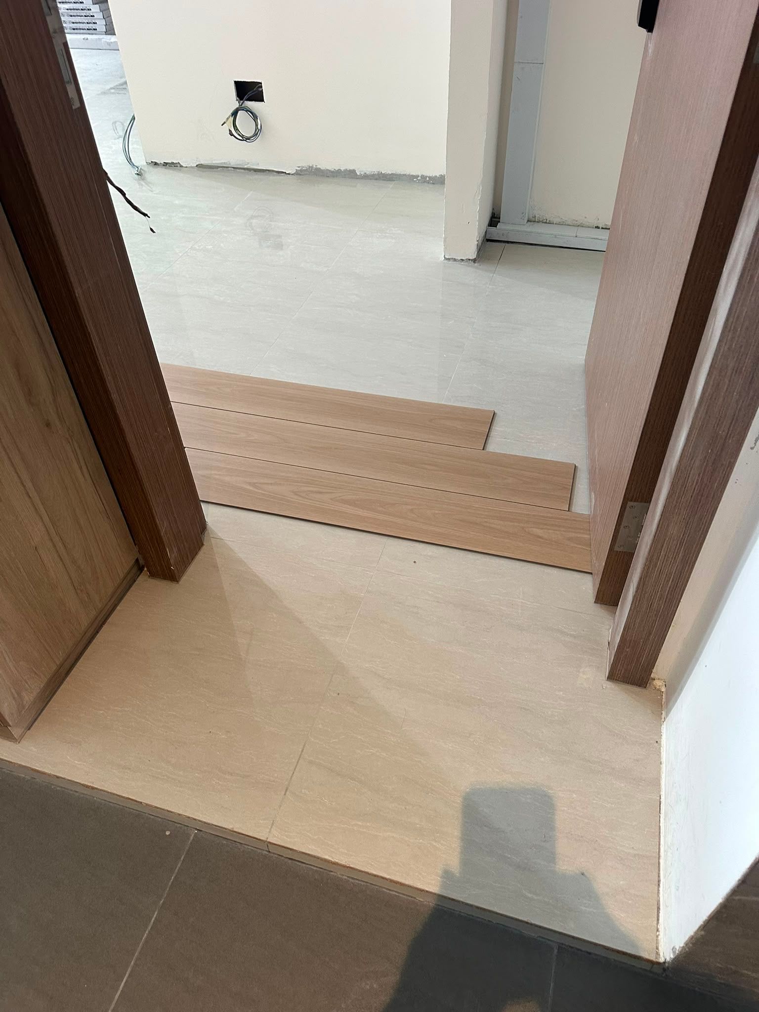 Vinyl sample planks across a doorway showing direction over grey and light tiles