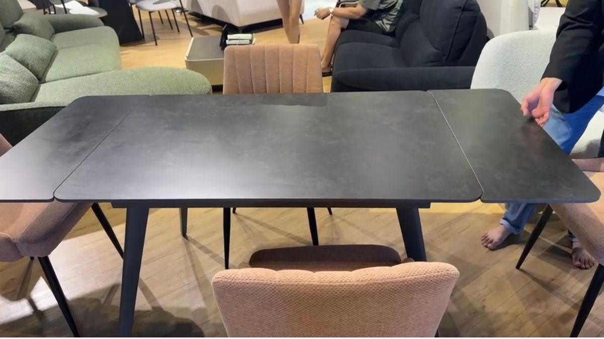 Dark extendable dining table with peach channel-back chairs, hand on the extension leaf at Homiest Living
