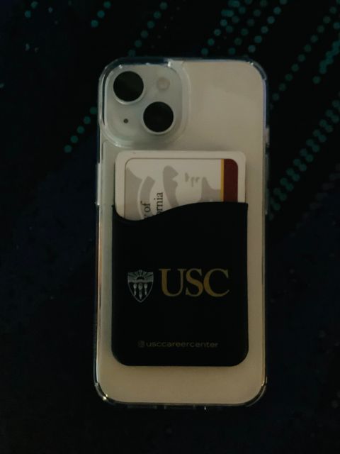 A photo of an iPhone 15 with a clear case and a stick on wallet.