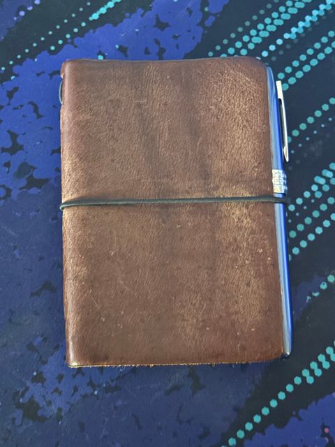 A photo of a passport size leather cover with notebooks inside of it along with a pen strapped to it.