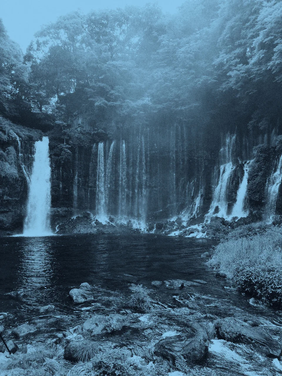 Waterfalls cascading down a wooded cliff.