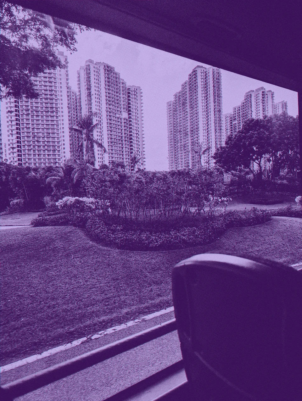 Apartment towers and gardens seen through a bus window.