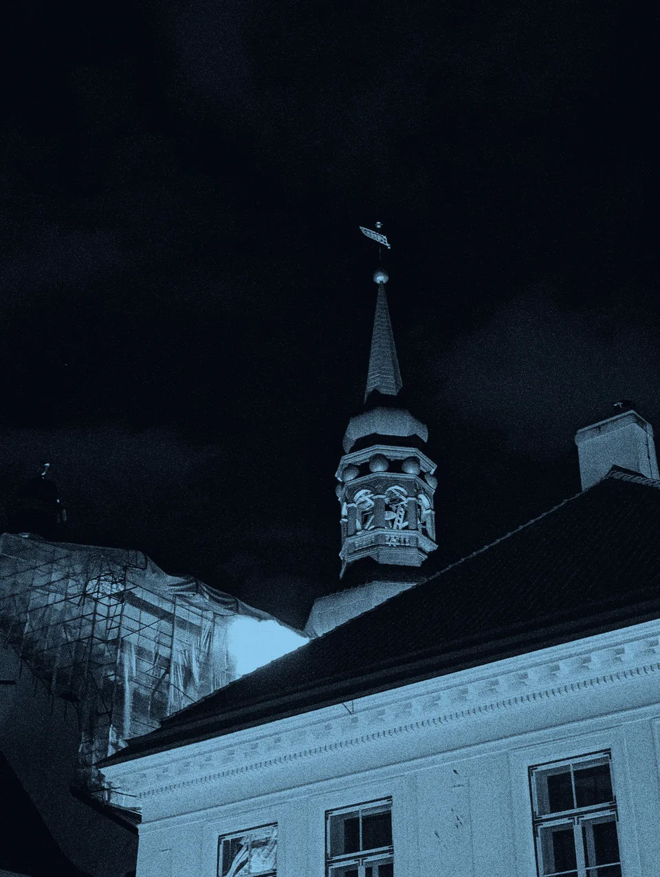 An illuminated spire above rooftops at night.