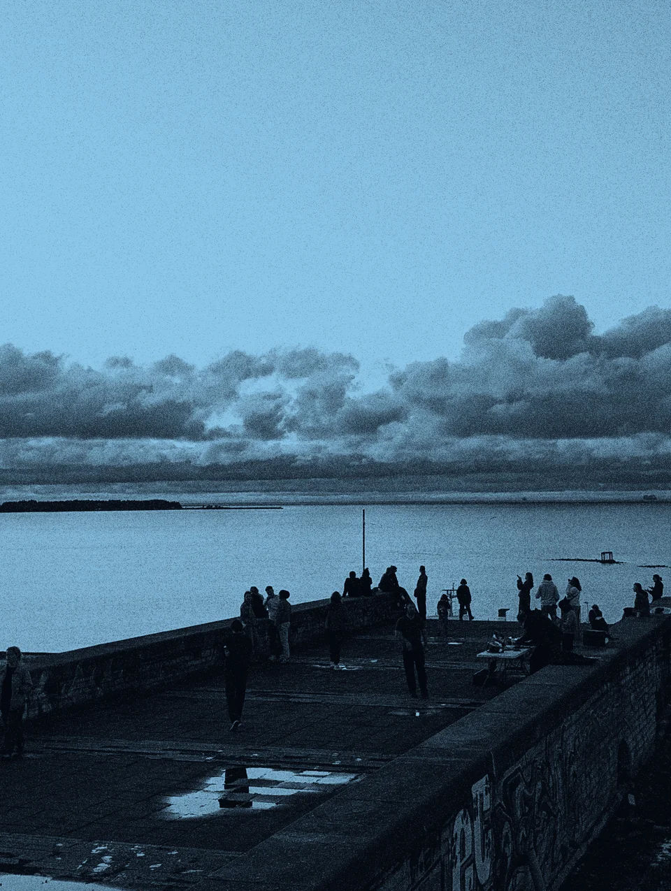 People on a waterfront terrace overlooking the sea.