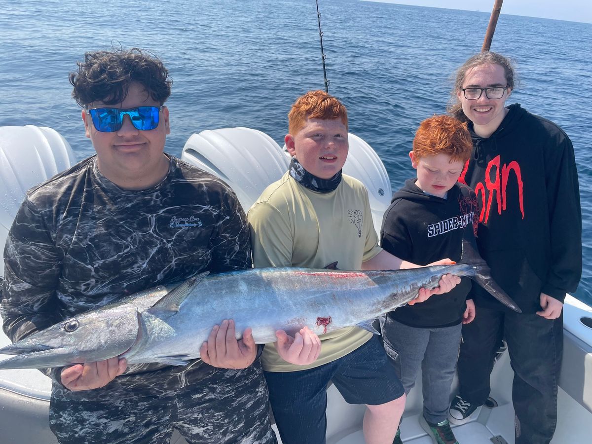 Teens fishing offshore in March holding a large Wahoo during March fishing