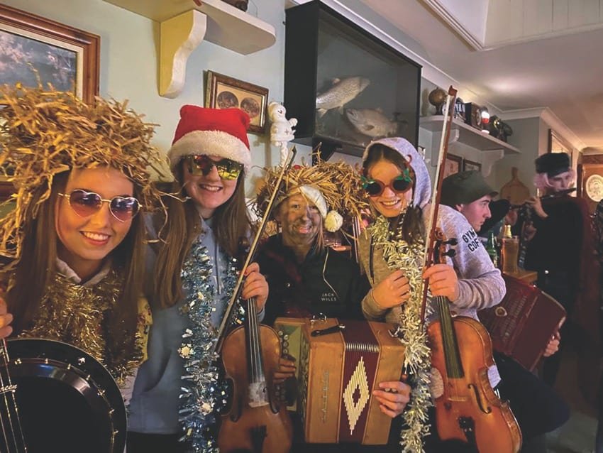 A group of musicians in costumes including sunglasses, a santa hat, tinsel and straw