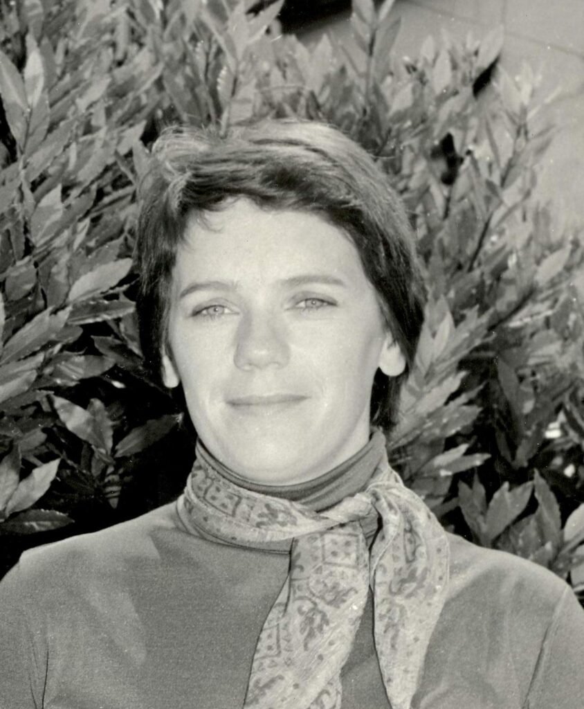 Black and white photo of a woman with short dark hair wearing a high neck top and a scarf tied round her neck