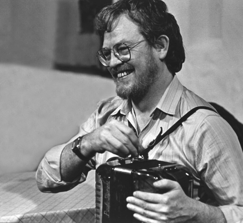 Black and white photo of a smiling man with glasses holding an accordian