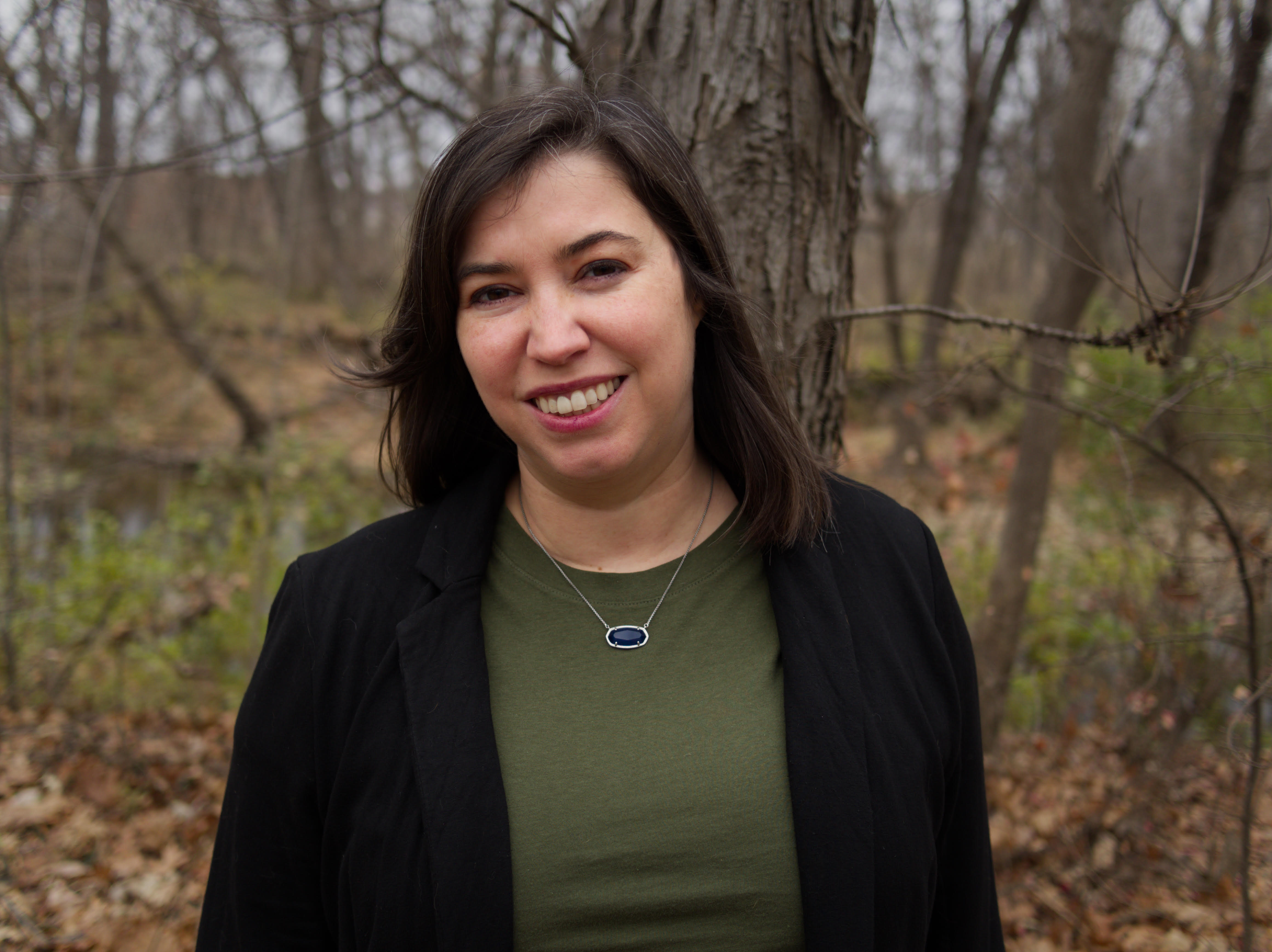 Portrait of the author, a lovely, brown-haired woman, outside in front of trees