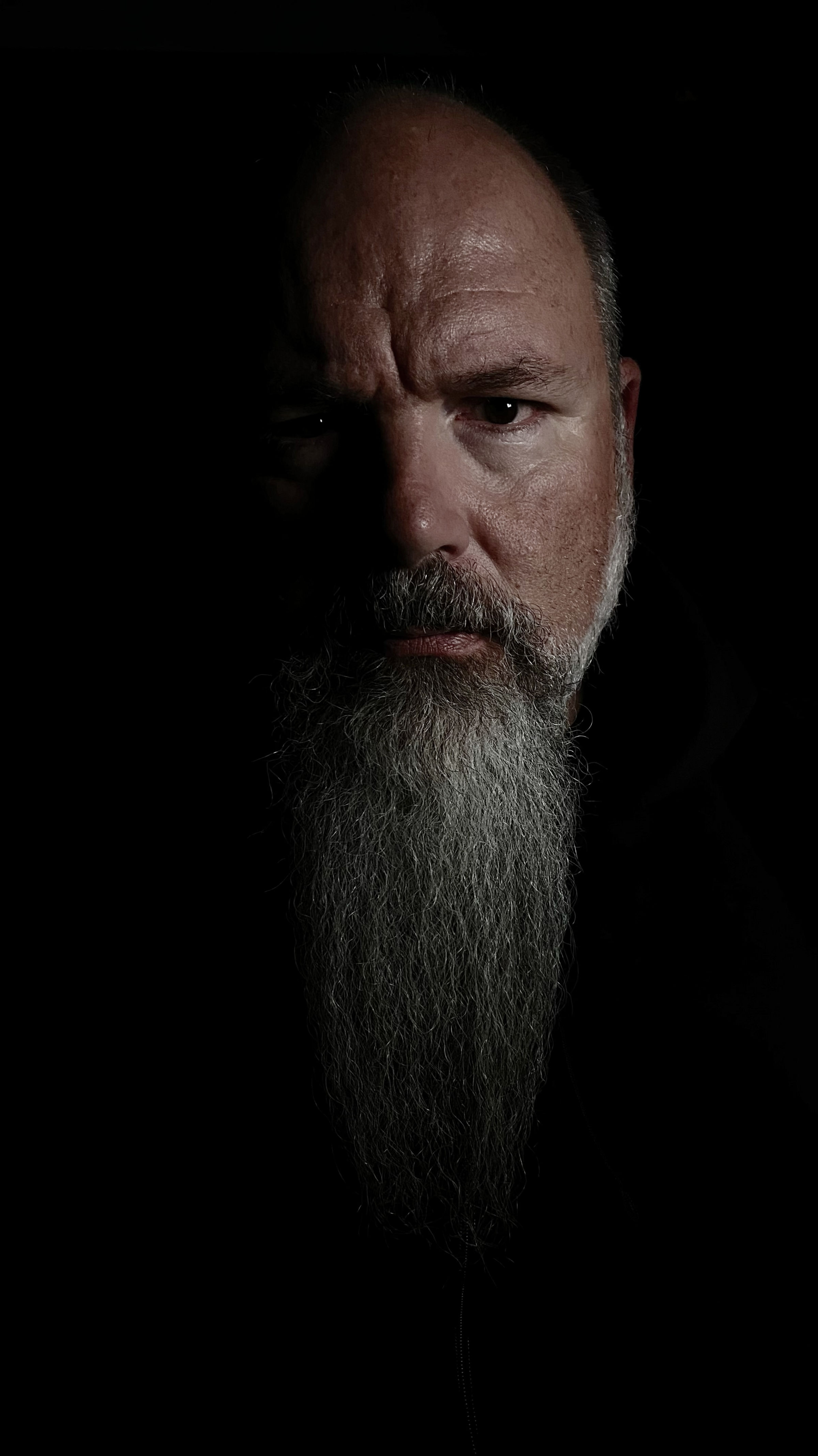 A scary looking bald man with an epic goatee in chiaroscuro, blending light and shadow.