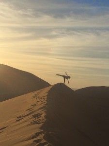 Young girl turning a cartwheel atop a sand dune against the twilight sky 