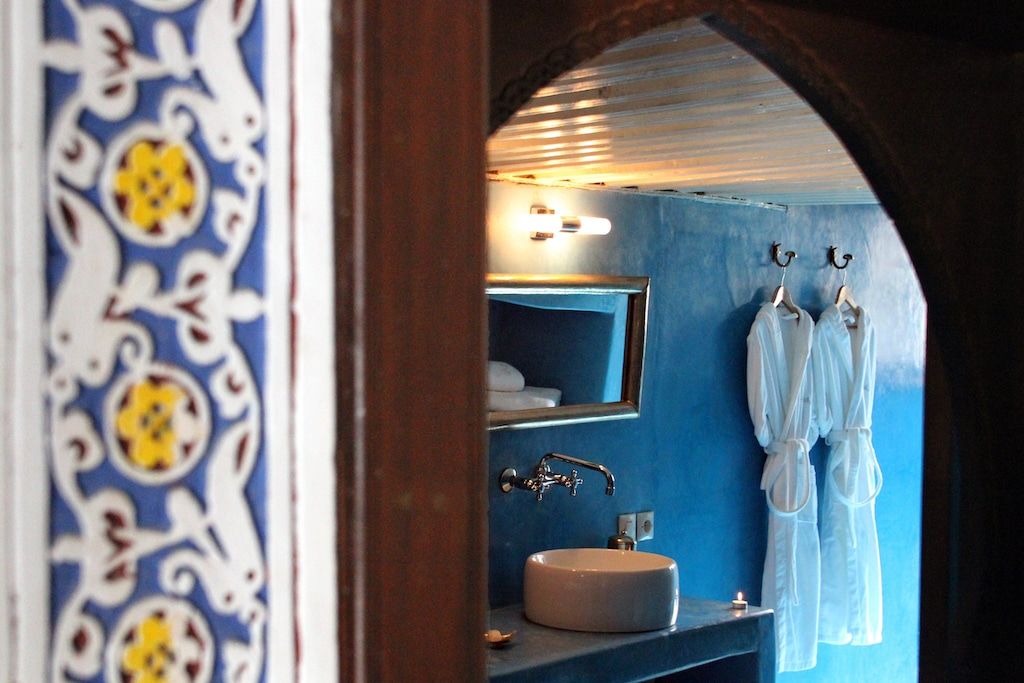 a framed view into a private bathroom with blue walls and two bathrobes hangin from hooks in the wall