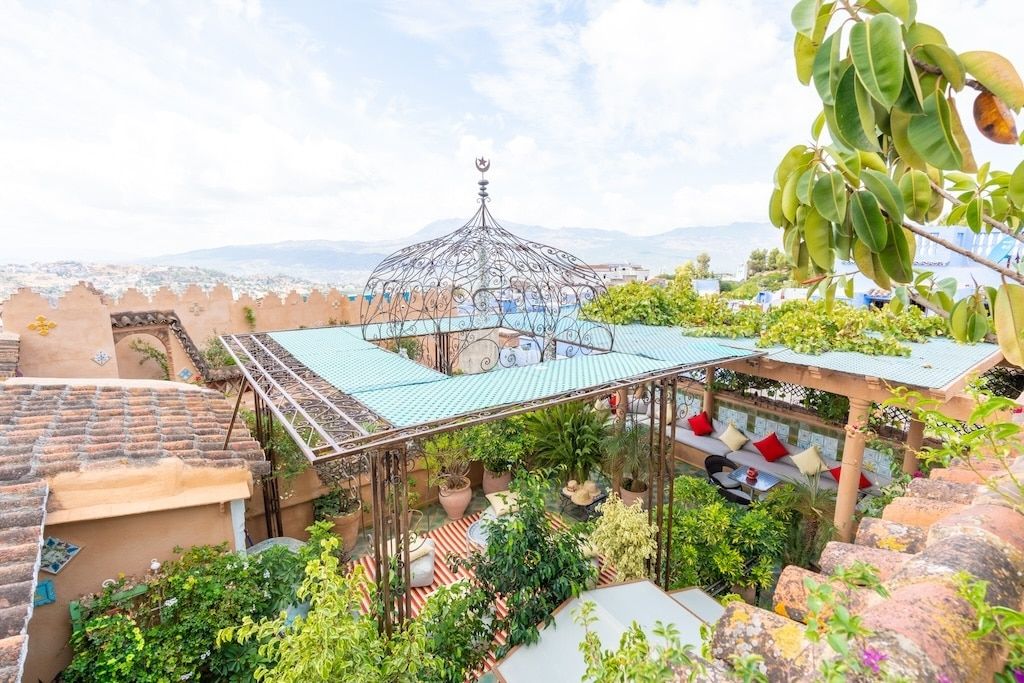 An aerial view of a terrace in a Moroccan riad, full of plants and spaces to rest. The terrace is surrounded by high walls ensuring privacy and safety