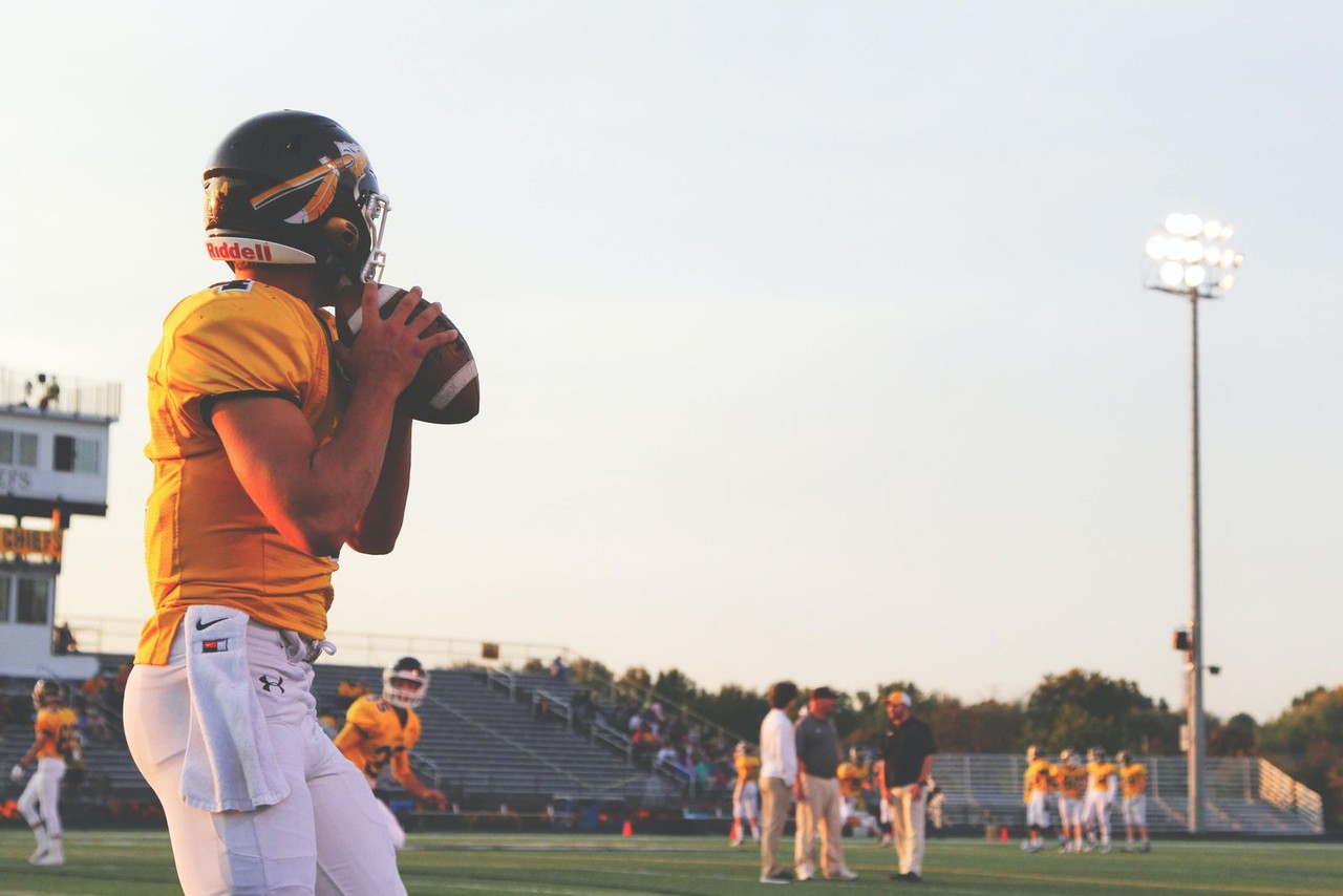 High school quarterback preparing to throw a long pass at a night football game