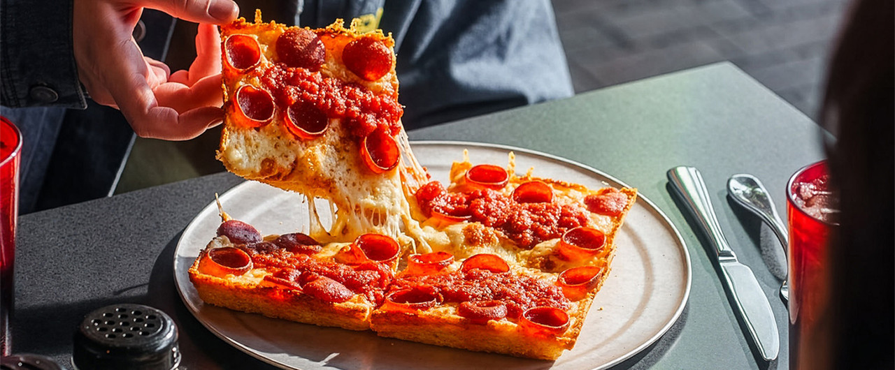 A slice of Detroit-style pepperoni pizza lifted from the plate