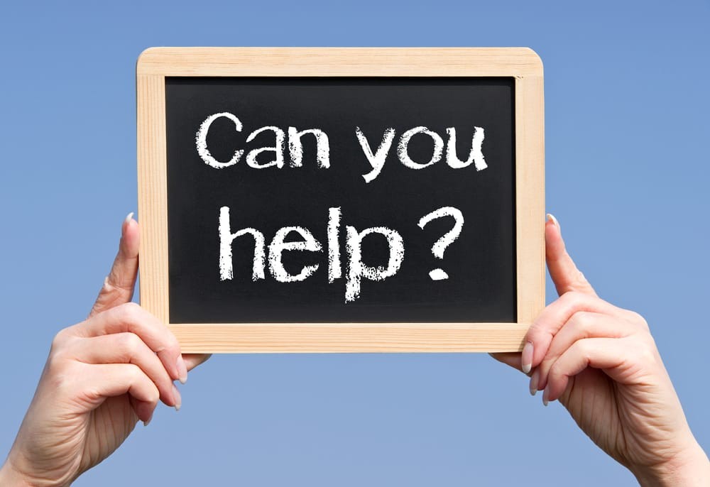 Small chalk board with the words 'can you help' written on it in chalk being held up by two hands with a blue sky background