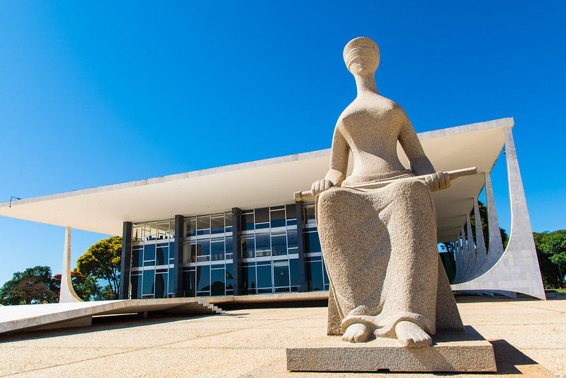 Imagem da fachada do STF tirada tendo como objeto principal a estátua da justiça e ao fundo o prédio do STF