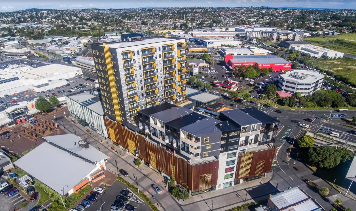 A photograph of the New Lynn town centre taken from in the air with the Library and Lynnmall in the centre left and apartments to the right. Redpaths and the New World supermarket can be seen in the background with Blockhouse Bay behind