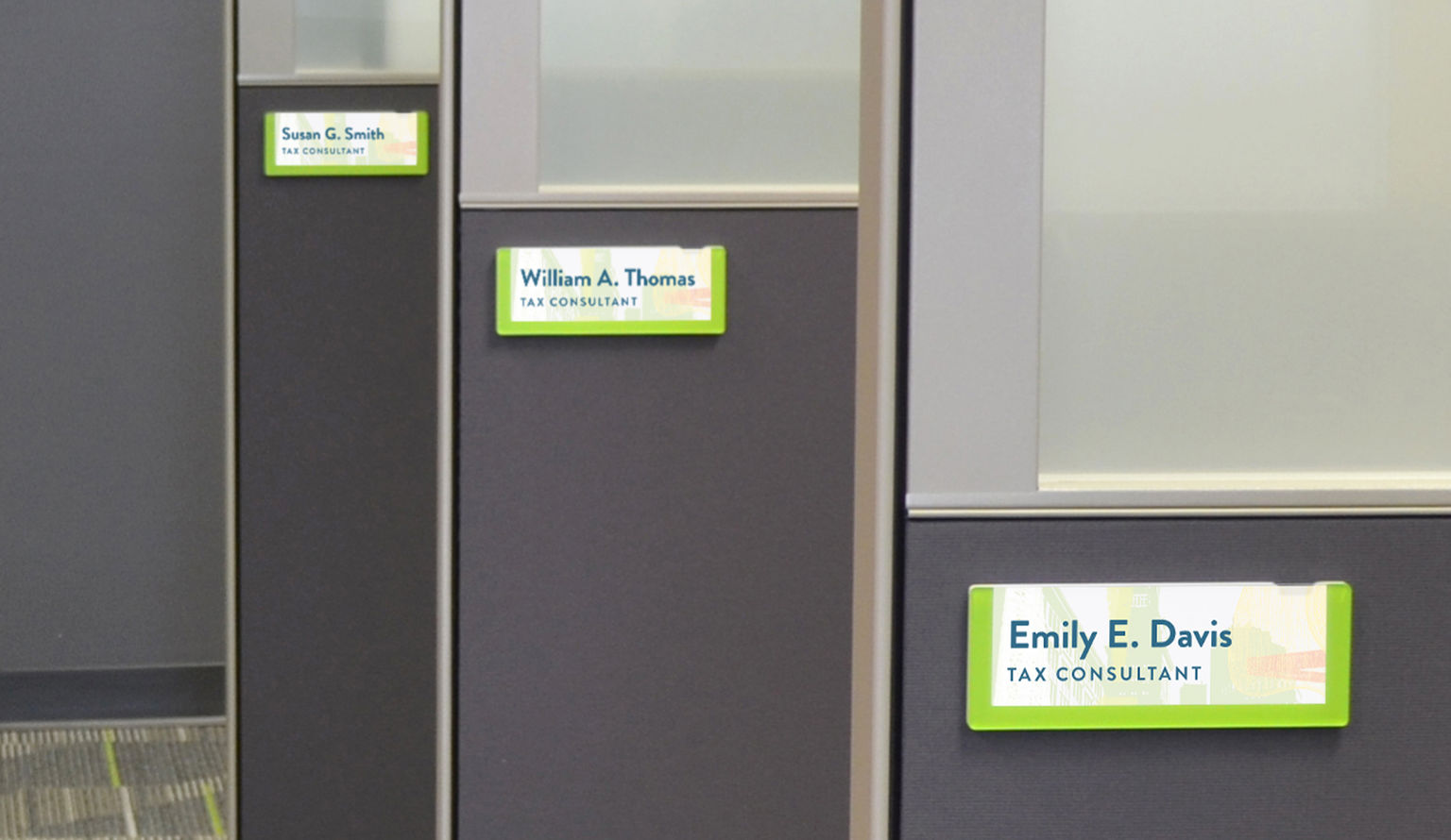 A row of office cubicles with personalized workstation nameplates with branded graphics.