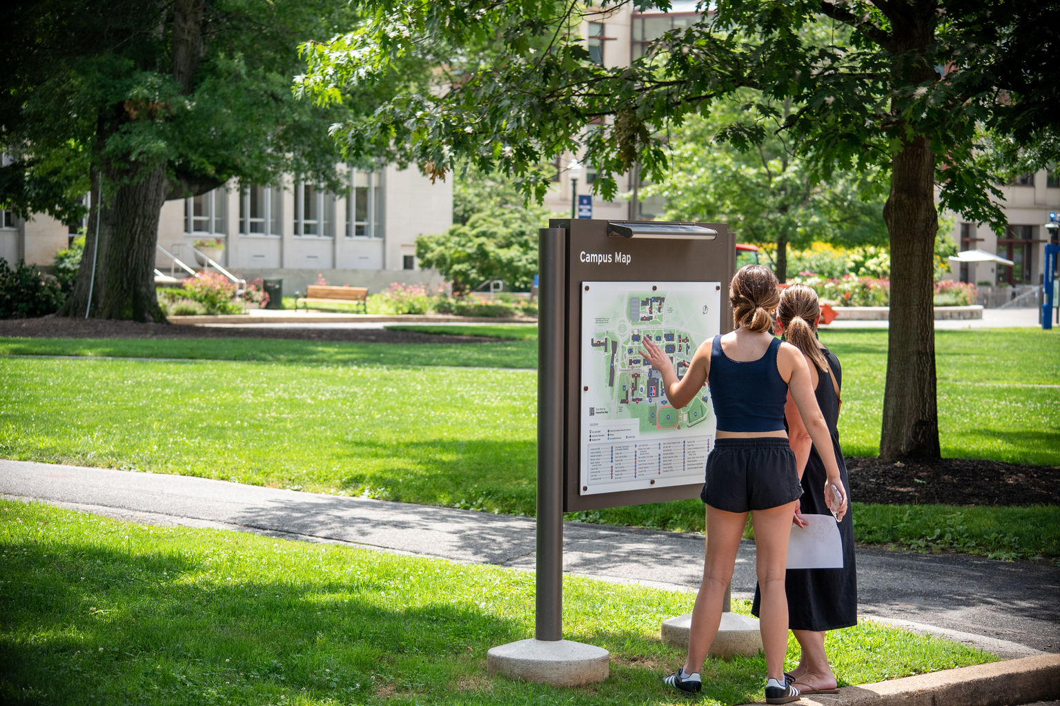A student and mother navigating a campus map on an exterior post and panel sign on a college campus.