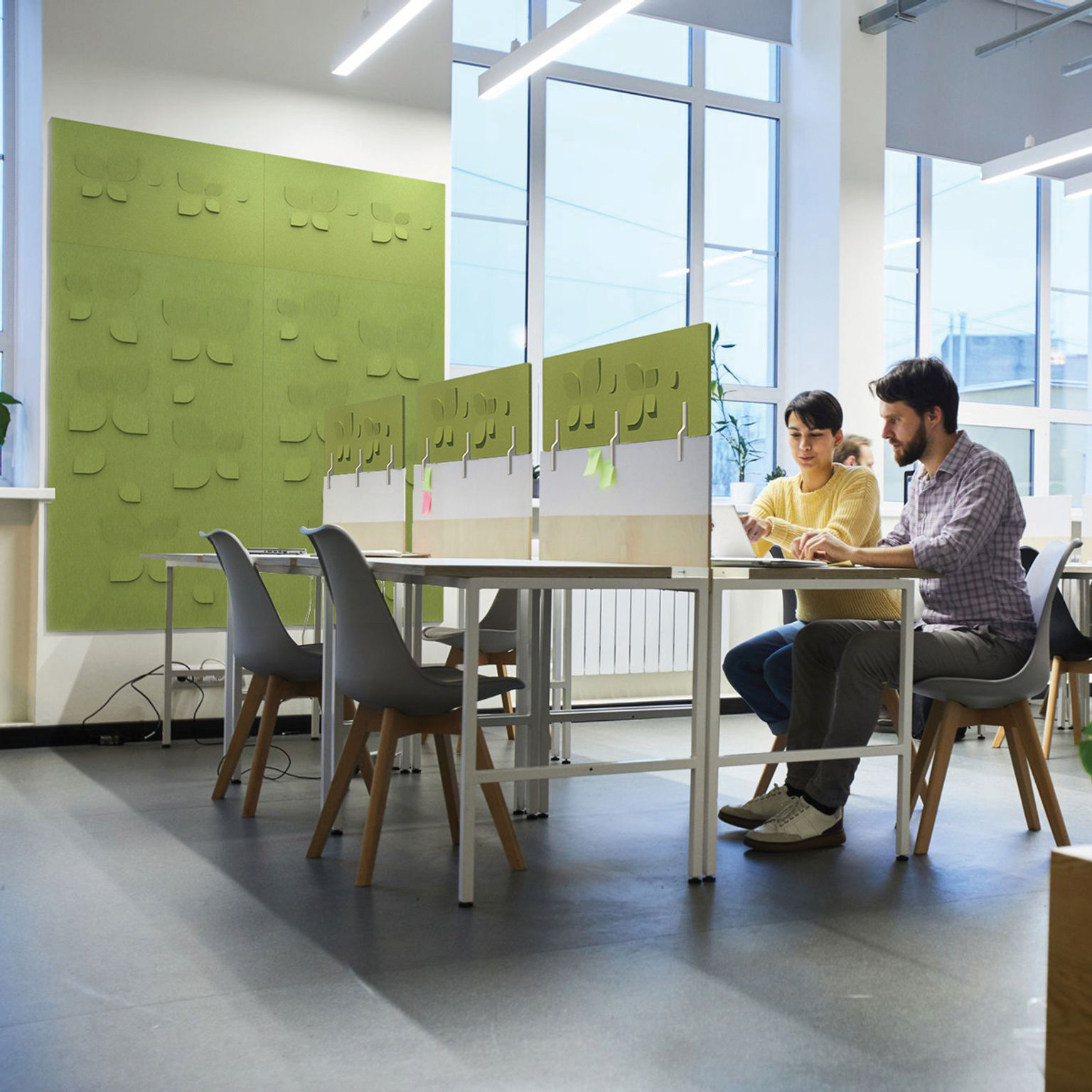 Several people work in a collaborative space featuring green acoustic wall panels and workstation stackers with a dimensional push-through pattern.