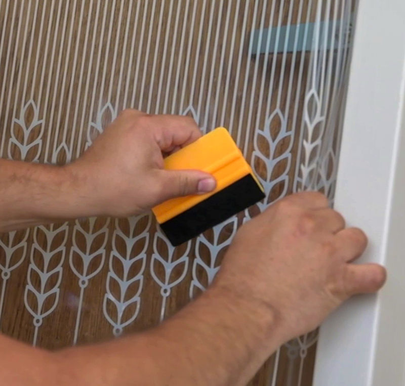 A detail photo of an installer applying amplify window film with a squeegee to an interior glass surface.