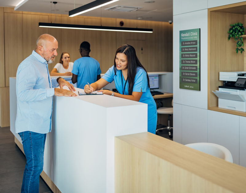 A man at a reception desk in a doctors office with a changeable magnetic directory on the wall