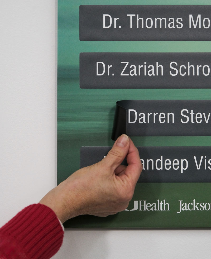 A hand pulling back the corner of a removable name on a directory in a doctors office