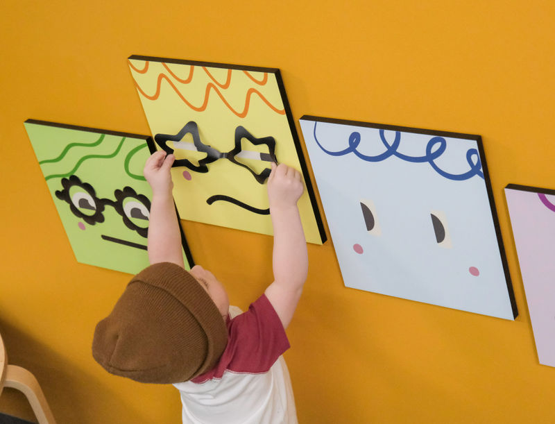 A boy interacting with multiple magnetic layers of a playful wall display in an optometrist office