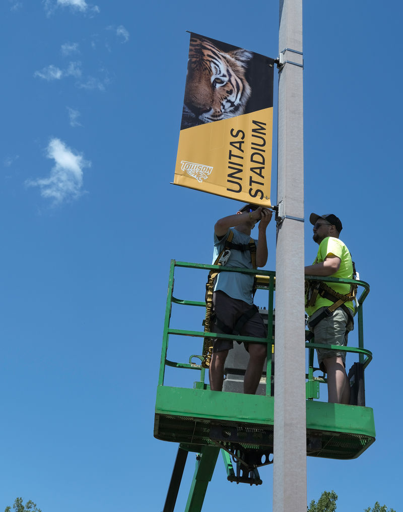 Two men on a lift installing an exterior pole banner.