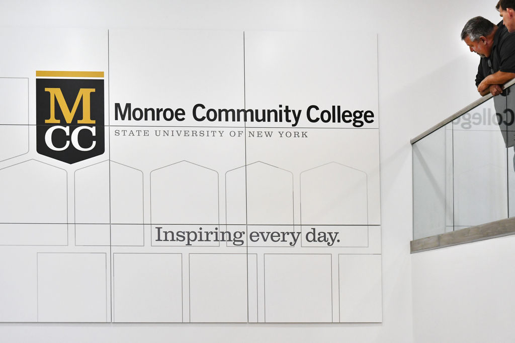 Two men admiring a large custom printed moxie graphic panel installation on an interior second-floor wall of a higher education building.