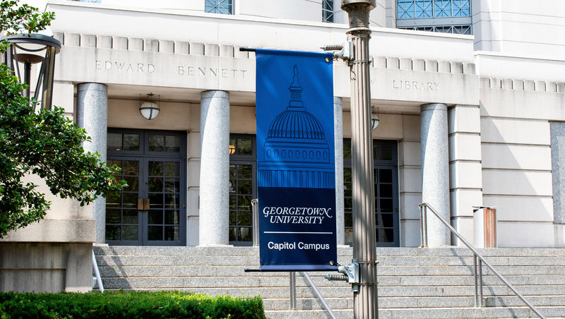 An exterior pole banner in front of a historic building in a college campus.