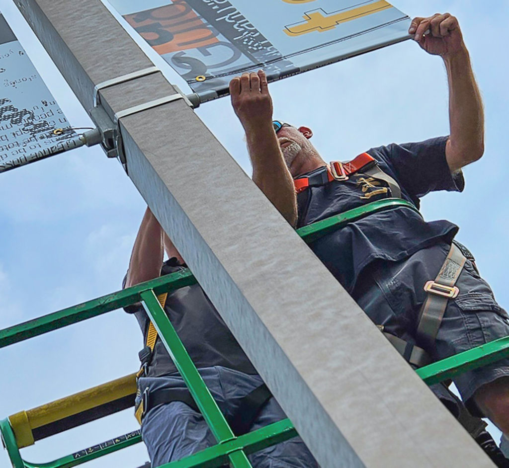 Two Takeform field service members installing exterior banners on a lift.