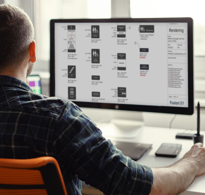 An experiential graphic designer working on a computer with signage renderings on screen.