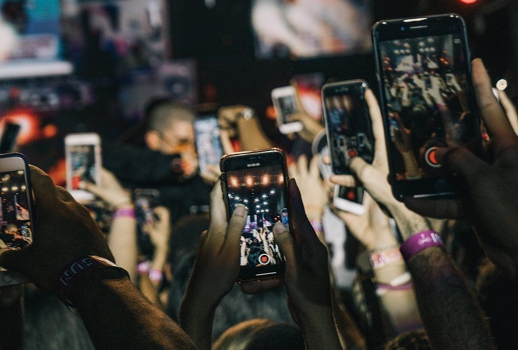 Several people in a crowd hold their smartphones aloft to capture a picture