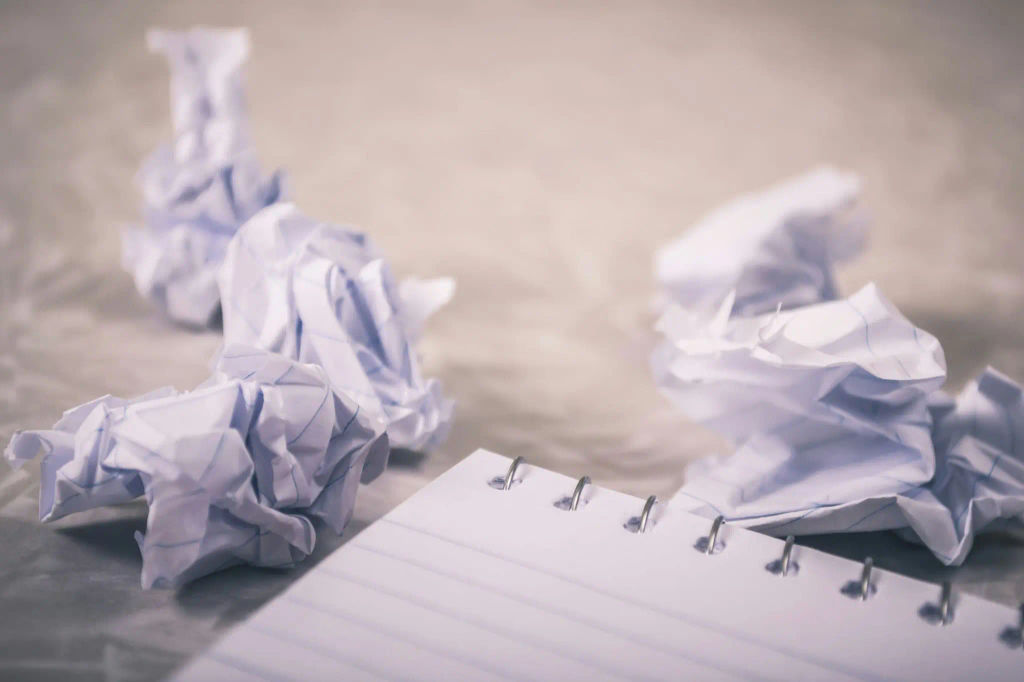 Crumpled paper balls beside a blank notebook, symbolizing common mistakes and rewrites.