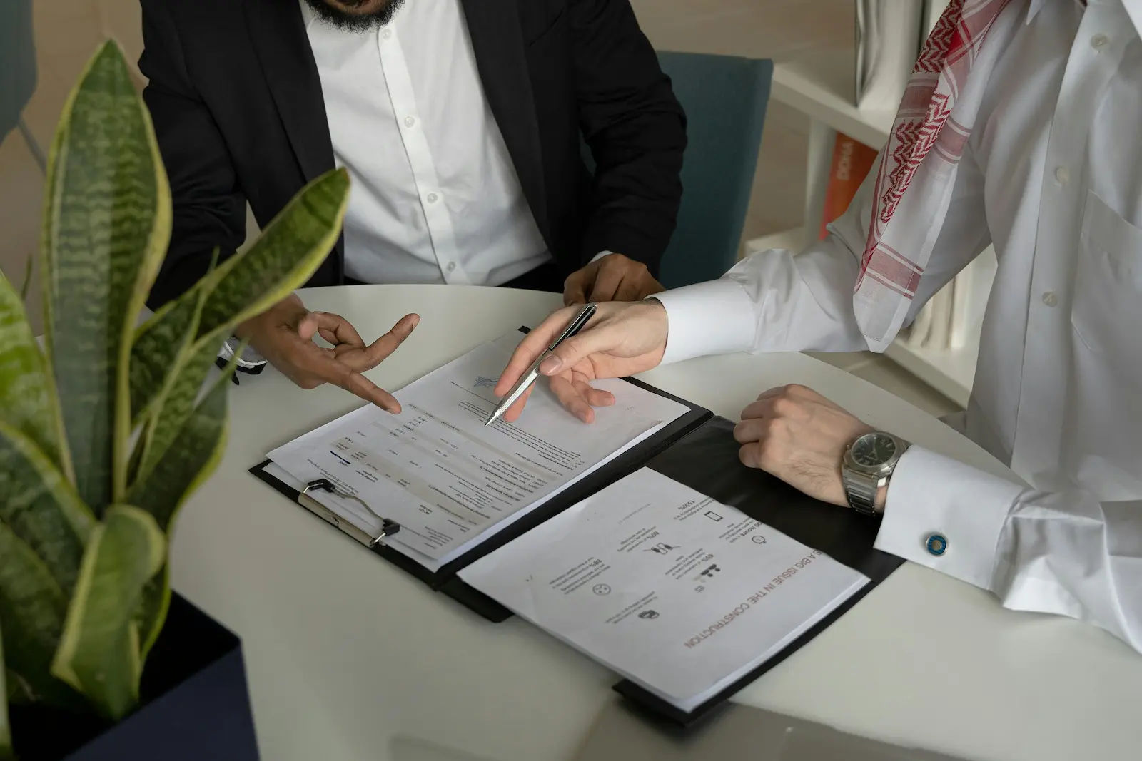 Close-up of hands gesturing over a document on a clipboard, as two people discuss details before signing