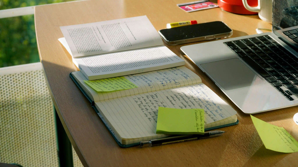 Workspace with laptop, phone, and handwritten notes used to prepare a cease and desist template
