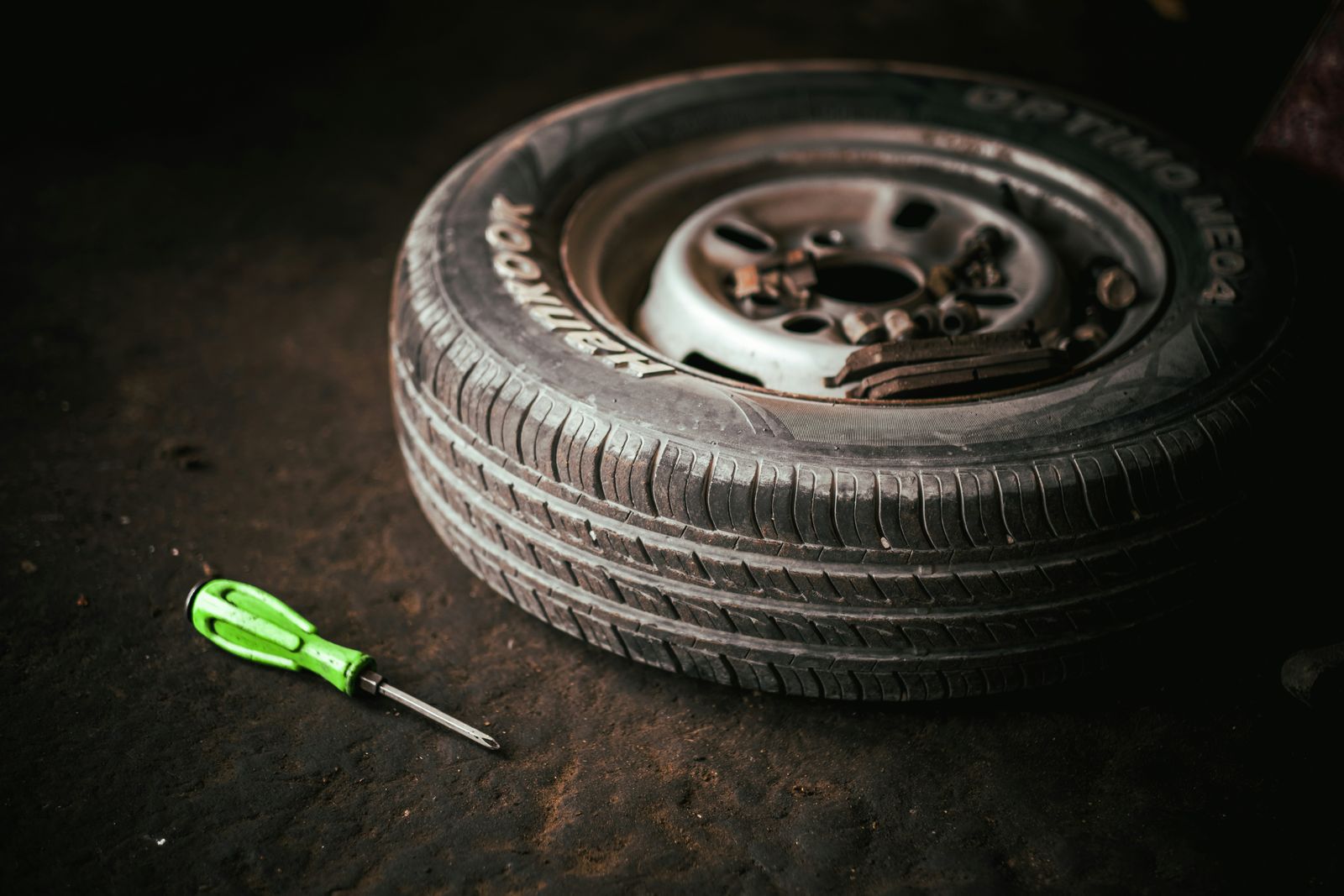 Car tire on a workshop floor next to a green screwdriver.