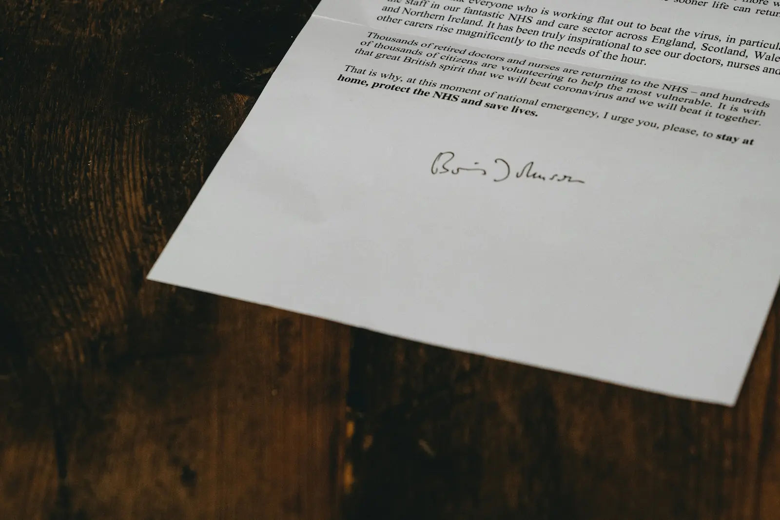 Signed paperwork lying on a dark wood surface, with the signature line visible near the bottom.